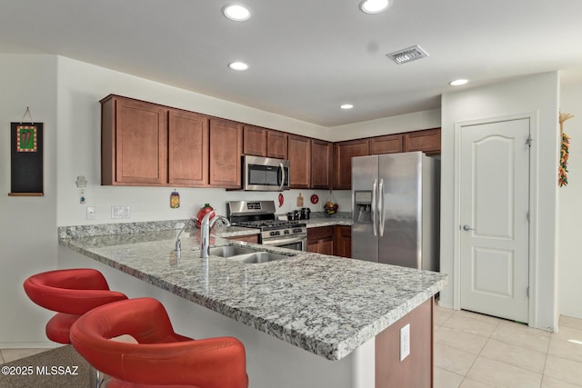 kitchen with kitchen peninsula, light stone counters, stainless steel appliances, sink, and light tile patterned floors