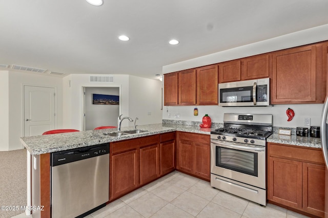 kitchen with light stone countertops, stainless steel appliances, kitchen peninsula, and sink