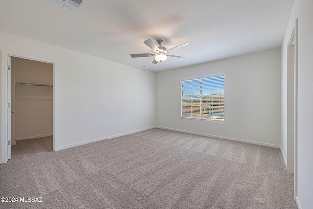 unfurnished bedroom featuring a closet, a walk in closet, light colored carpet, and ceiling fan