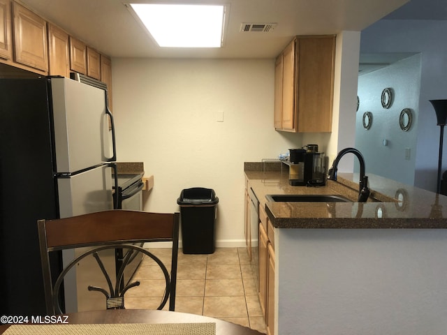 kitchen featuring dark stone counters, sink, light tile patterned floors, light brown cabinets, and white fridge