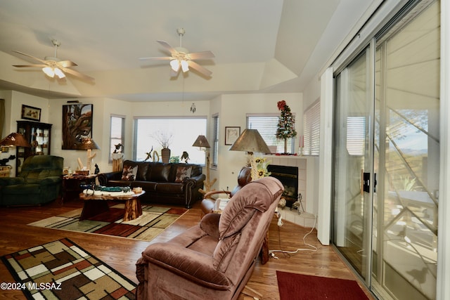 living room with hardwood / wood-style floors, a tray ceiling, ceiling fan, and a tiled fireplace