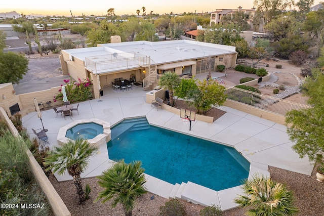 pool at dusk featuring an in ground hot tub and a patio