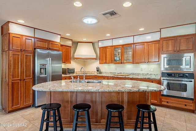 kitchen with a kitchen bar, a kitchen island with sink, stainless steel appliances, and custom exhaust hood