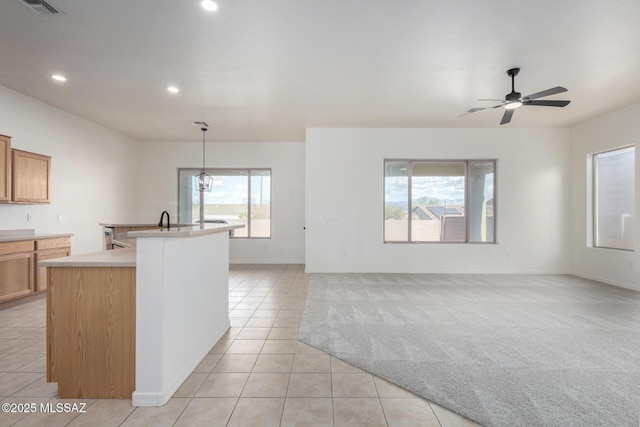 kitchen with pendant lighting, light colored carpet, ceiling fan, and a kitchen island with sink