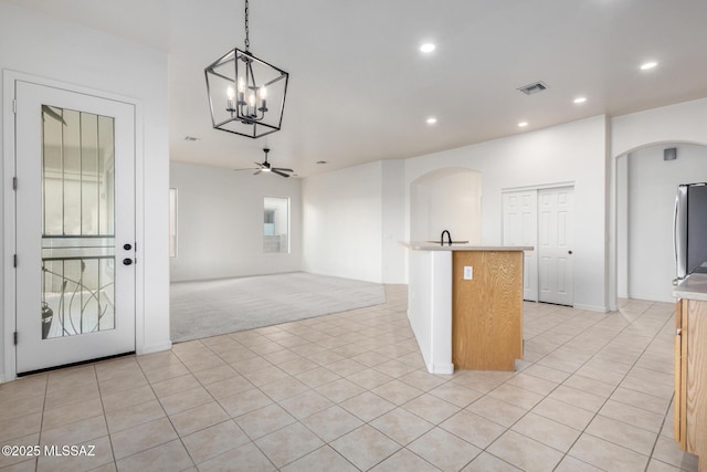 kitchen featuring light tile patterned flooring, decorative light fixtures, an island with sink, stainless steel fridge, and ceiling fan