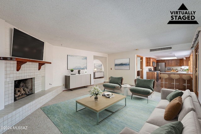 living room with light colored carpet, a textured ceiling, and a tile fireplace