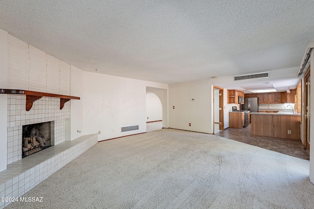 unfurnished living room featuring a tiled fireplace, light carpet, and a textured ceiling