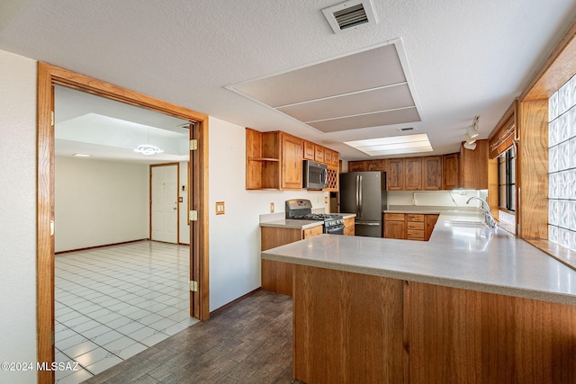 kitchen with sink, a textured ceiling, dark hardwood / wood-style flooring, kitchen peninsula, and stainless steel appliances