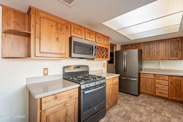 kitchen with light wood-type flooring, a textured ceiling, and appliances with stainless steel finishes