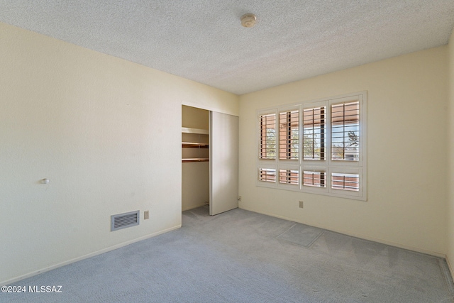 unfurnished bedroom featuring a textured ceiling, light carpet, and a closet