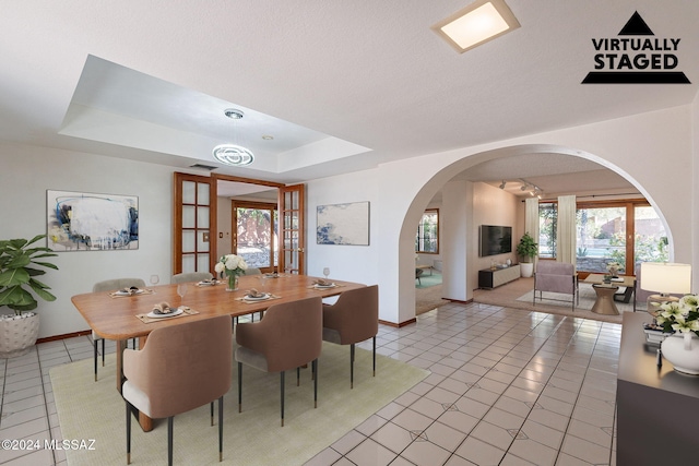 dining area with a tray ceiling, french doors, light tile patterned floors, and a textured ceiling