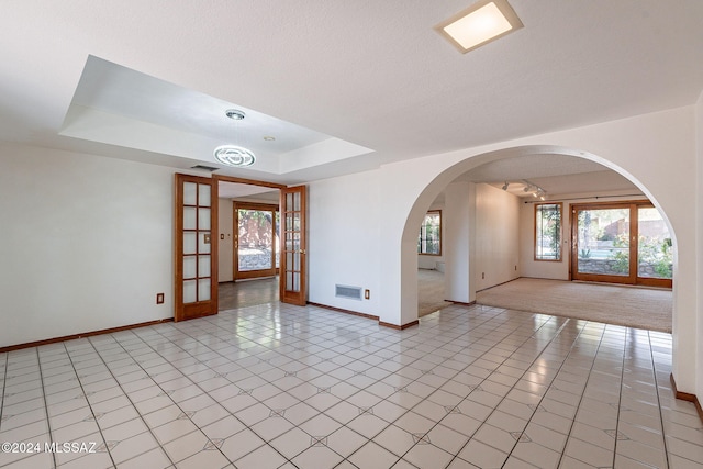 empty room with french doors, a notable chandelier, a textured ceiling, a tray ceiling, and light tile patterned floors