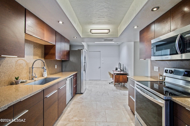 kitchen with sink, light stone counters, tasteful backsplash, a textured ceiling, and stainless steel appliances