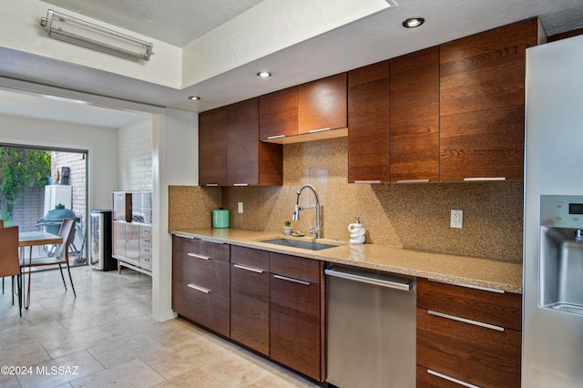 kitchen featuring sink, refrigerator with ice dispenser, backsplash, stainless steel dishwasher, and light stone countertops