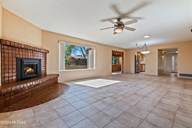 unfurnished living room with ceiling fan, light tile patterned flooring, and a brick fireplace