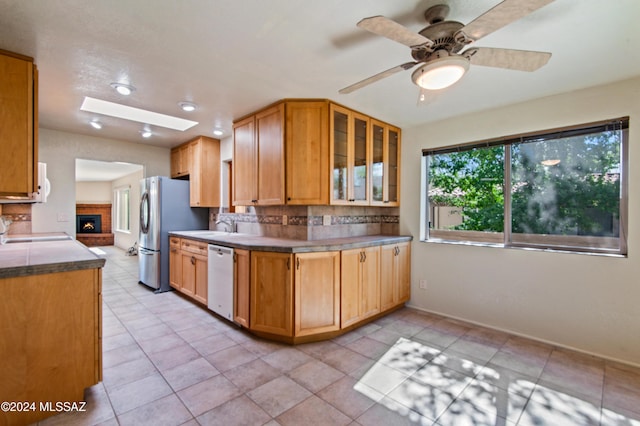 kitchen with decorative backsplash, a skylight, a brick fireplace, white appliances, and ceiling fan