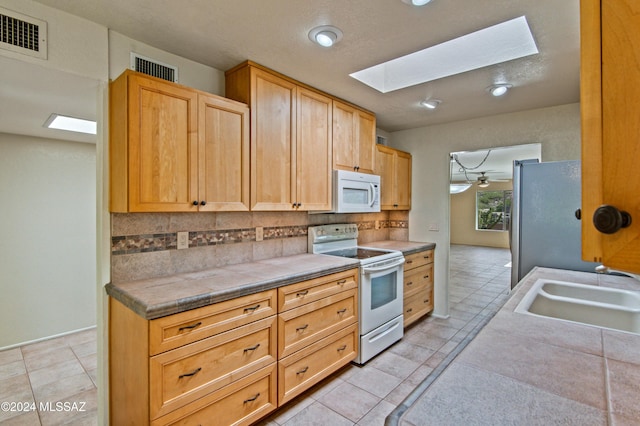 kitchen with backsplash, a skylight, white appliances, ceiling fan, and sink