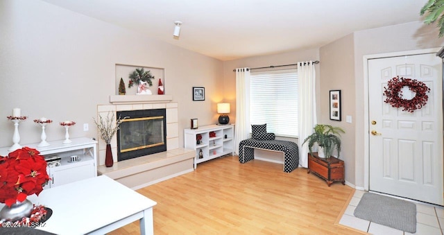 living room with a tiled fireplace, light hardwood / wood-style floors, and vaulted ceiling