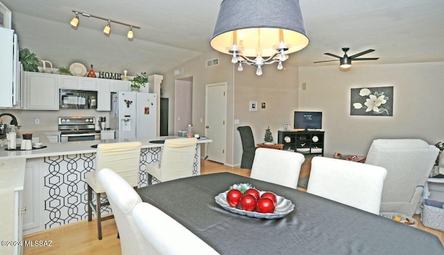 dining room with ceiling fan with notable chandelier, light wood-type flooring, and lofted ceiling