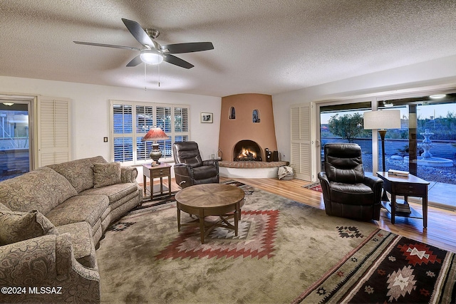 living room with ceiling fan, wood-type flooring, a fireplace, and a textured ceiling