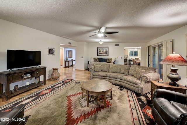 living room with ceiling fan, a textured ceiling, and light wood-type flooring