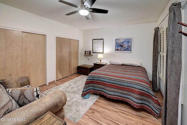 bedroom with ceiling fan, two closets, a textured ceiling, and light wood-type flooring