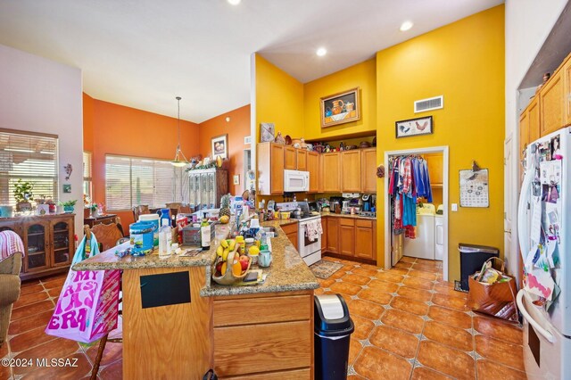 kitchen with hanging light fixtures, light stone counters, white appliances, washer and clothes dryer, and light tile patterned flooring