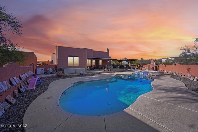 pool at dusk featuring an in ground hot tub and a patio