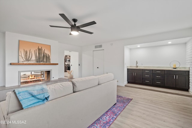 living room with a multi sided fireplace, light hardwood / wood-style flooring, and ceiling fan