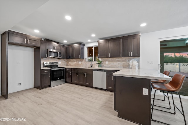 kitchen with kitchen peninsula, appliances with stainless steel finishes, backsplash, a kitchen breakfast bar, and light hardwood / wood-style flooring