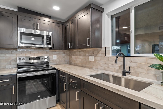 kitchen featuring light stone countertops, appliances with stainless steel finishes, backsplash, dark brown cabinetry, and sink