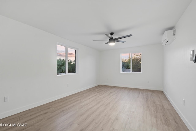 empty room featuring a wall unit AC, ceiling fan, a healthy amount of sunlight, and light wood-type flooring