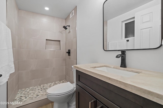 bathroom with a tile shower, vanity, and toilet