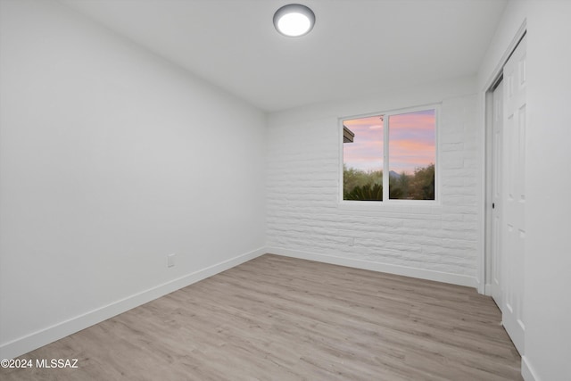 unfurnished room with light wood-type flooring and brick wall