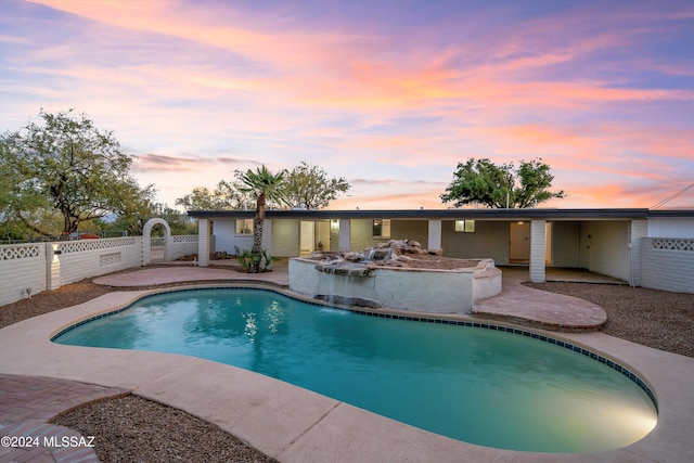 pool at dusk featuring a patio area and pool water feature