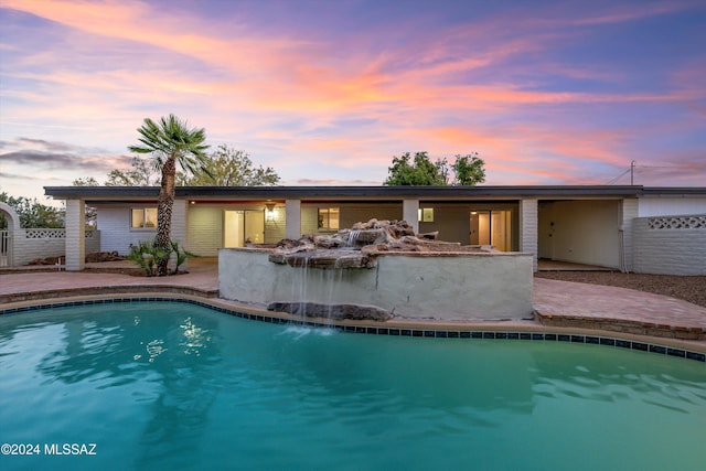 pool at dusk featuring pool water feature and a patio area