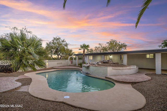 pool at dusk featuring pool water feature and a patio