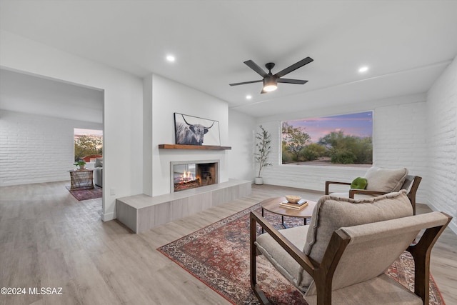 living room with ceiling fan, light hardwood / wood-style floors, and brick wall