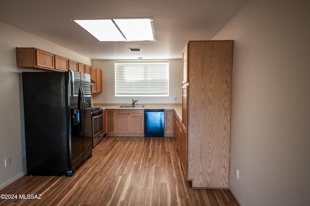 kitchen with stainless steel appliances, a skylight, light hardwood / wood-style floors, and sink