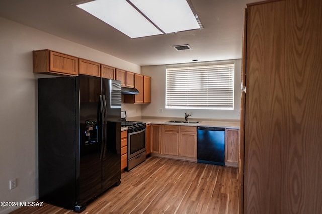 kitchen with sink, a skylight, light hardwood / wood-style flooring, and black appliances