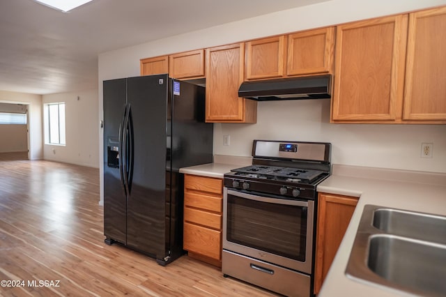 kitchen featuring sink, black fridge with ice dispenser, light hardwood / wood-style flooring, and stainless steel gas range