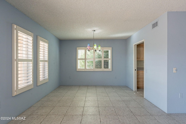 unfurnished dining area with a wealth of natural light, light tile patterned floors, a chandelier, and a textured ceiling