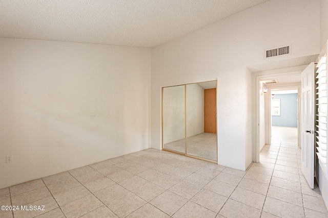 unfurnished bedroom featuring light tile patterned flooring, a textured ceiling, high vaulted ceiling, and a closet