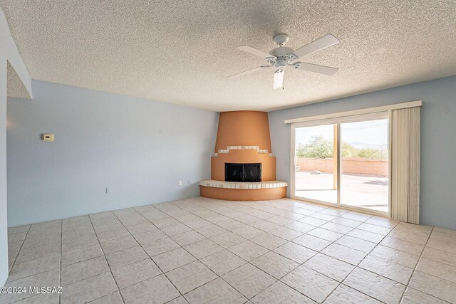 unfurnished living room with ceiling fan, a fireplace, light tile patterned flooring, and a textured ceiling