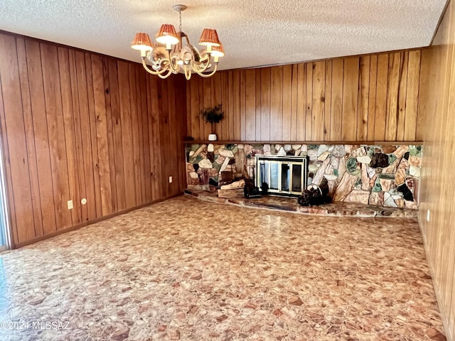 interior space with a textured ceiling, wood walls, a fireplace, and a chandelier