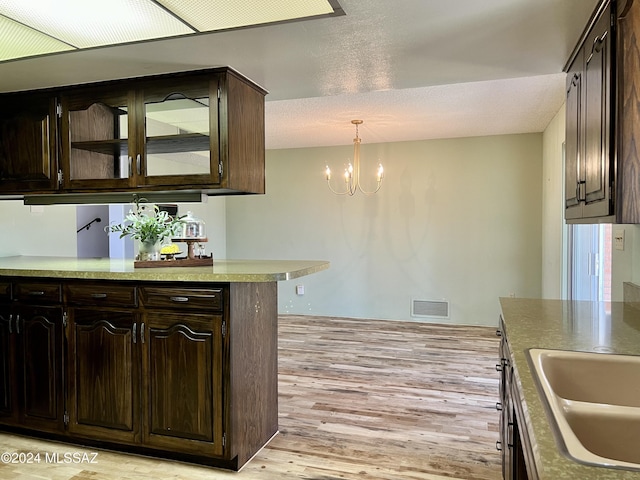 kitchen with dark brown cabinetry, sink, a notable chandelier, pendant lighting, and light wood-type flooring