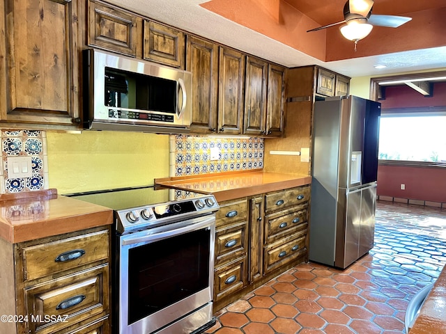 kitchen with tile patterned flooring, decorative backsplash, ceiling fan, a textured ceiling, and stainless steel appliances