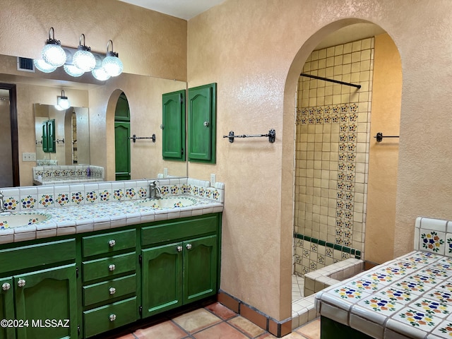 bathroom with tile patterned flooring, a tile shower, and vanity