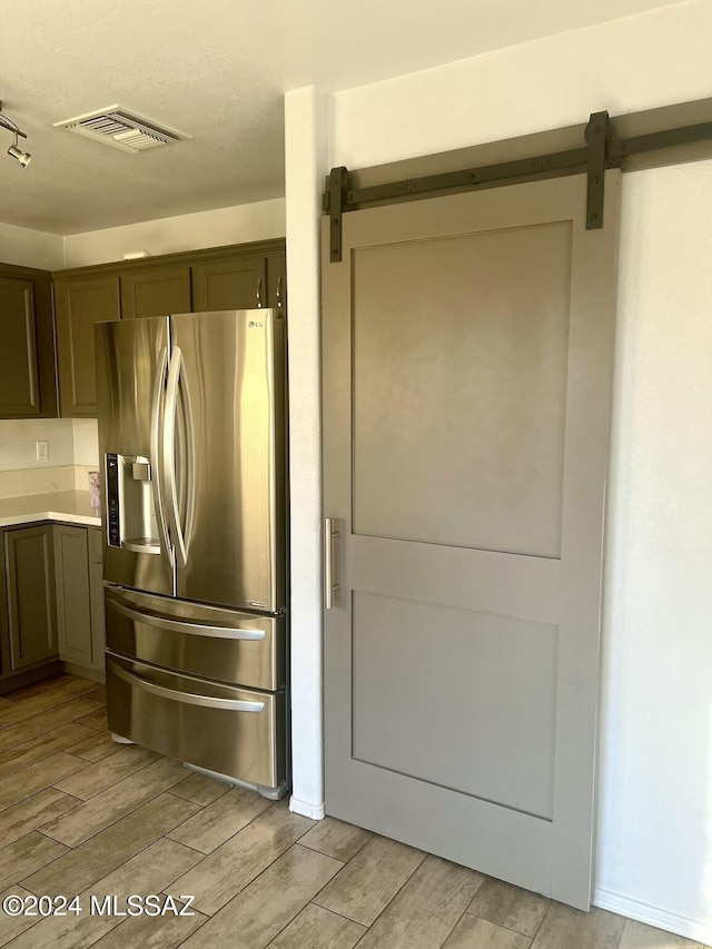 kitchen with a barn door, stainless steel fridge, light hardwood / wood-style flooring, and dark brown cabinets