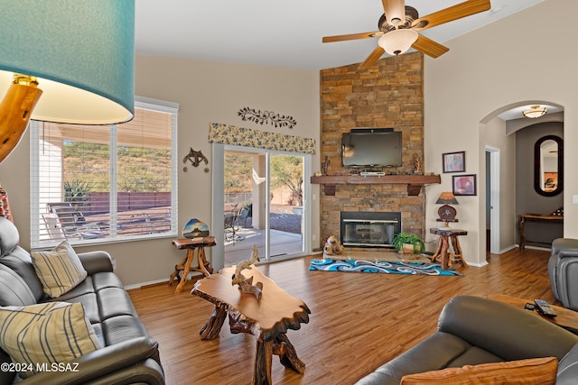 living room featuring a stone fireplace, ceiling fan, light hardwood / wood-style floors, and vaulted ceiling